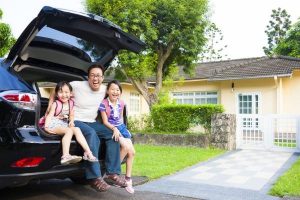 father-and-daughters-sitting-in-back-of-car-outside-house